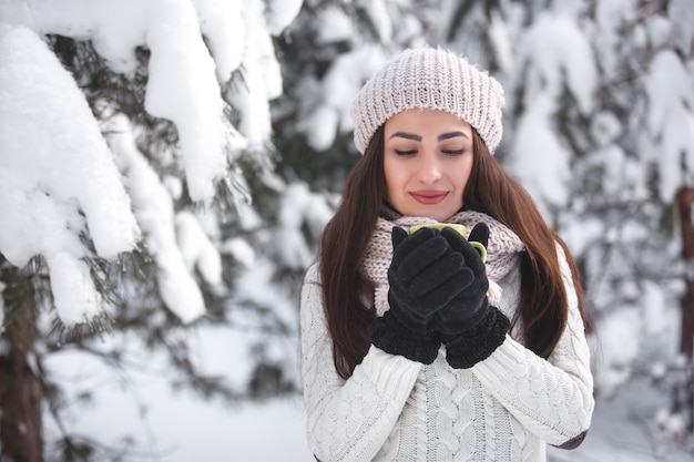 Mooi meisje in het bos op de winterachtergrond met theekop. Mooie vrolijke vrouw het drinken koffie in openlucht. Sluit omhoog portret van een mooie dame