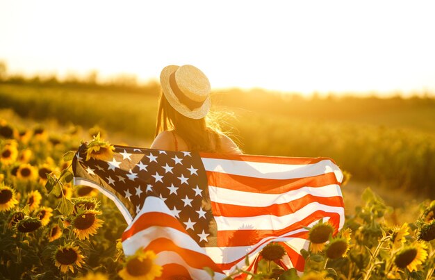 Mooi meisje in hoed met Amerikaanse vlag in een zonnebloemveld 4 juli Onafhankelijkheidsdag