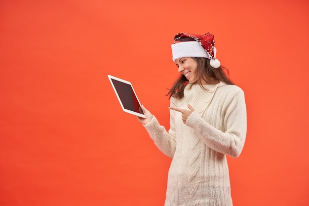 Mooi meisje in kerstman hoed glimlachend gelukkig met haar tablet cadeau op oranje achtergrond