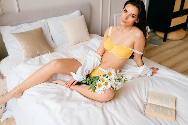 Mooi meisje in ondergoed en shirt poseren in slaapkamer met bloemen
