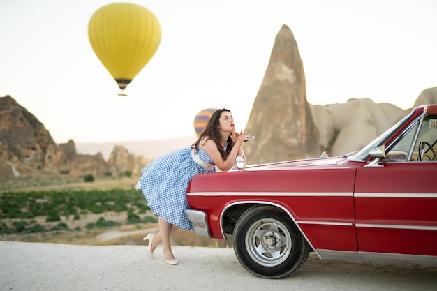 Mooi meisje in retro stijl poseren in de buurt van een vintage rode cabriolet auto op de achtergrond van ballonnen in Cappadocië