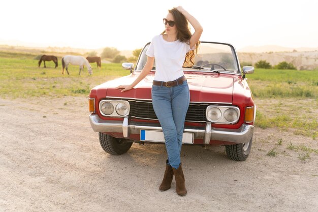 Foto mooi meisje in retro stijl poseren in de buurt van vintage rode cabriolet auto