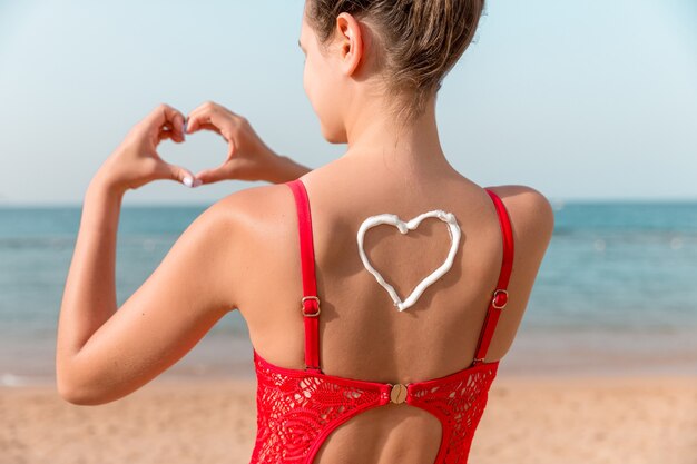 Mooi meisje in rode zwembroek heeft sunblock in de vorm van een hart aan de achterkant op het strand.