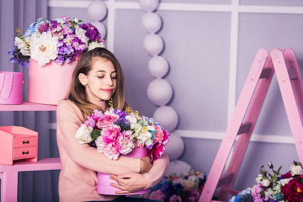 Mooi meisje in spijkerbroek en roze trui in studio met decor van bloemen in manden.