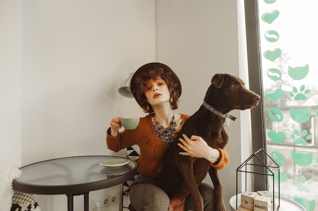 Mooi meisje in stijlvolle kleding, zittend in een licht café met een kopje koffie in haar hand