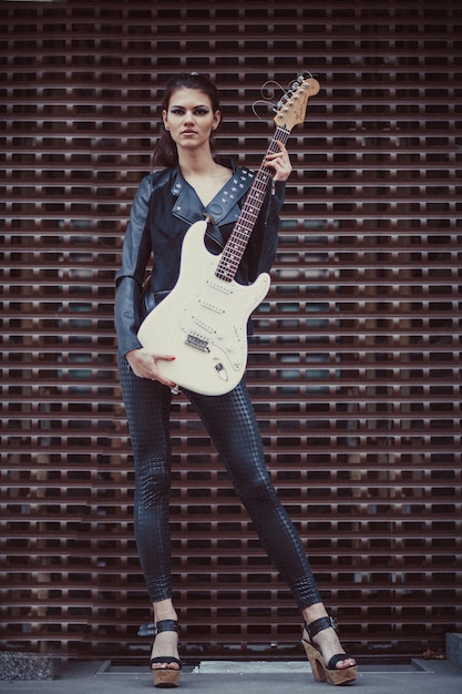 Mooi meisje in zwarte kleding poseert met elektrische gitaar