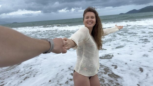 Mooi meisje, jonge, gelukkige, positieve vrouw leidt een man die haar hand vasthoudt. Volg haar naar het zomerstrand.