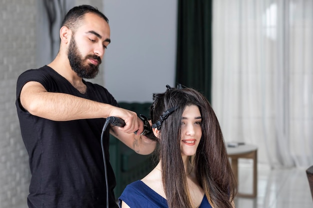 Mooi meisje lacht en kijkt naar de spiegel terwijl Kapper haar haar vormgeeft Foto van hoge kwaliteit