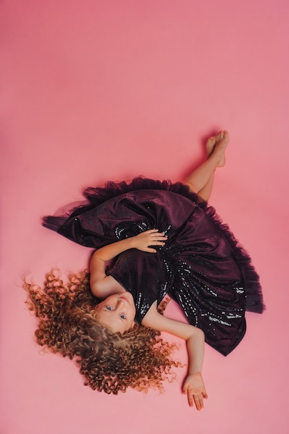 mooi meisje liggend in zwarte jurk op roze achtergrond in studio