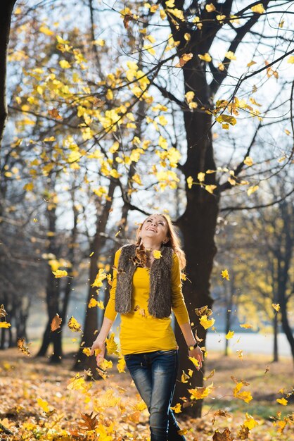 Mooi meisje loopt in het herfstpark met gele gevallen bladeren