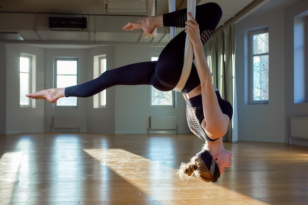 Mooi meisje luchtfoto yoga trainer toont medutiruet op hangende lijnen ondersteboven in een yogaruimte Concept yoga flexibel lichaam gezonde levensstijl fitness