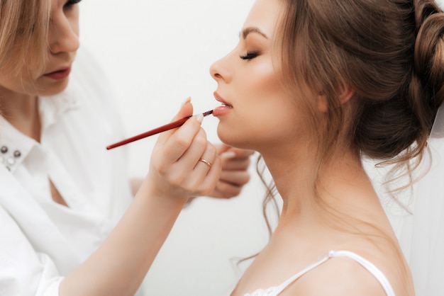 Mooi meisje make-up artiest maakt make-up en schildert haar lippen in een professionele schoonheidssalon