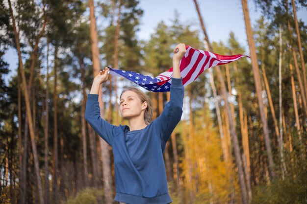 Mooi meisje met amerikaanse vlag. amerikaanse vlag in handen op warm zomerbos