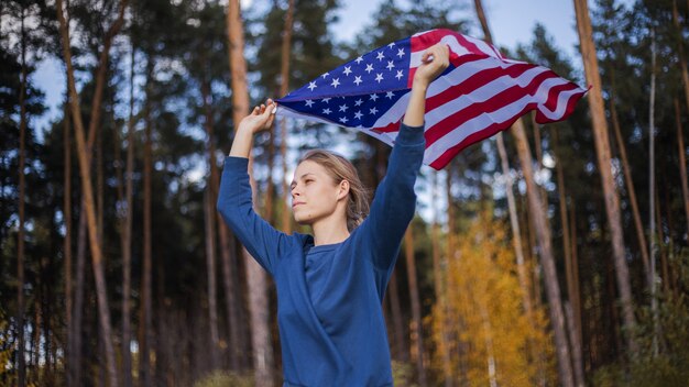 Mooi meisje met Amerikaanse vlag. Amerikaanse vlag in handen op warm zomerbos