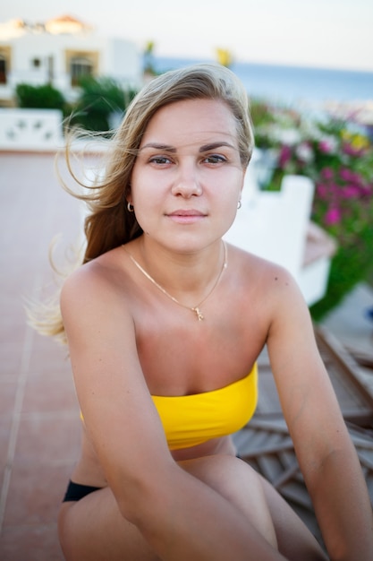 Mooi meisje met blond haar en in een geel zwempak ontspant op een terras tegen de zee