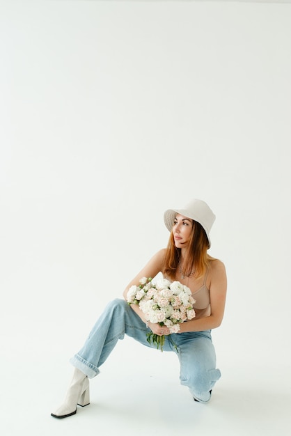 Mooi meisje met een boeket bloemen in een hoed en spijkerbroek