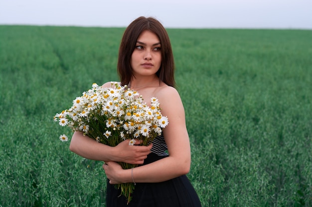 Mooi meisje met een boeket madeliefjes in een veld met bloemen.