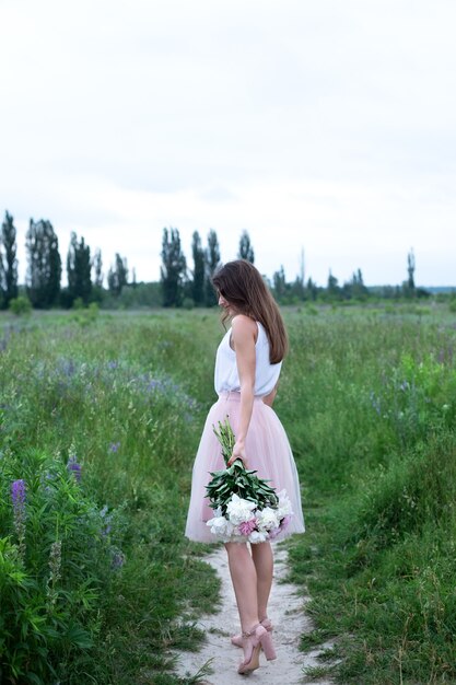 mooi meisje met een boeket roze pioenrozen bloemen achteraanzicht meisje met pioenrozen meisje in wilde bloemen