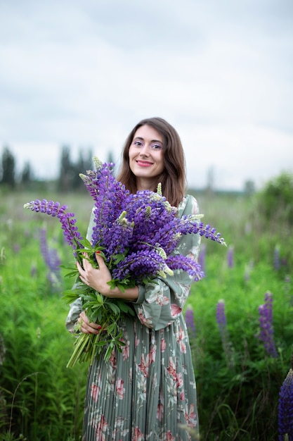 Mooi meisje met een boeket wilde bloemen Vrouw met een boeket lupine staat in bloemenveld