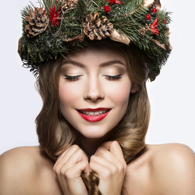 Mooi meisje met een krans van kerstboomtakken en kegels Nieuwjaarsafbeelding Schoonheid gezicht