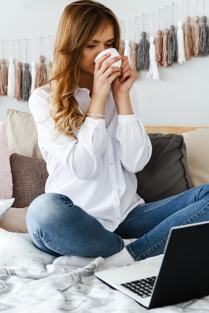 Mooi meisje met een laptop in de slaapkamer zit op het bed