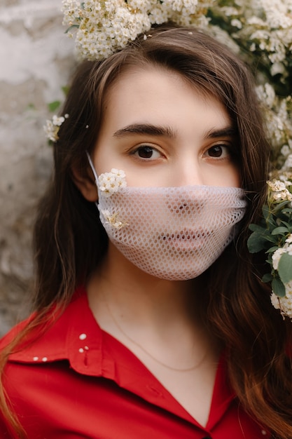 Mooi meisje met een medisch masker in bloeiende struiken