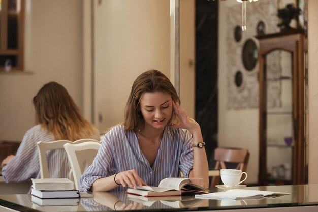 mooi meisje met lang blond haar in de eetkamer leest boeken en drinkt koffie