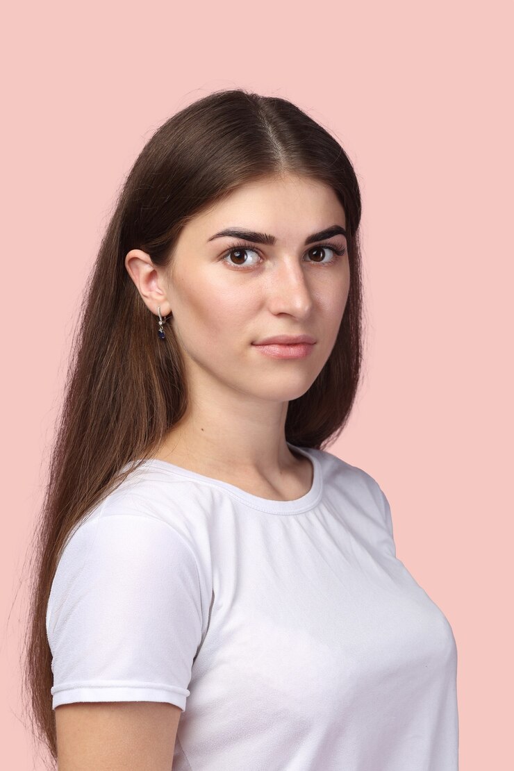 Foto mooi meisje met lang haar, gekleed in een wit t-shirt en poseren tegen lichtroze achtergrond. schattige brunette die er succesvol en professioneel uitziet en een positieve levenshouding heeft.