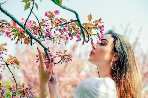 Mooi meisje met lang haar geniet van de schoonheid van de lenteaard in de buurt van de bloeiende sakuraboom.
