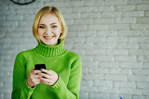 Mooi meisje met licht haar dragen groene trui zitten in café met mobiele telefoon, freelance concept, online winkelen, portret.