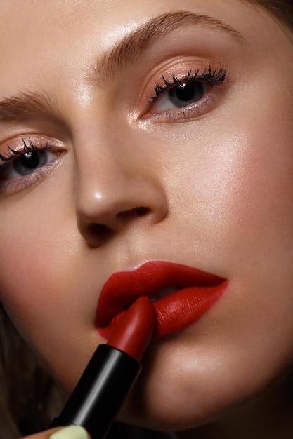 Mooi meisje met rode lippen en klassieke make-up met lippenstift in de hand Schoonheidsgezicht
