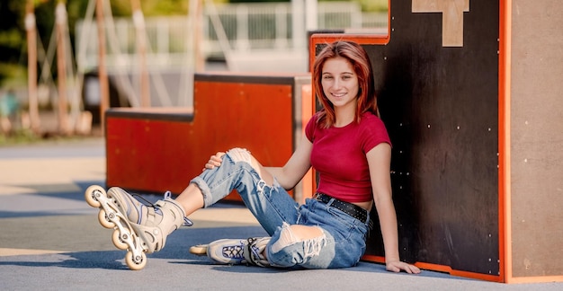 Mooi meisje met rolschaatsen die op de grond zitten en naar de camera kijken. Mooie vrouwelijke tiener skater stedelijk portret