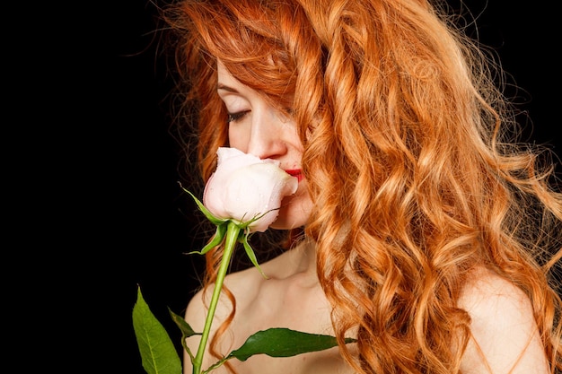 Mooi meisje met rood haar in een zwarte jurk met een roos op een zwarte achtergrond