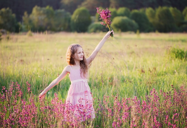 Mooi meisje met roze bloemen op de weide