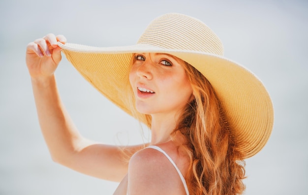 Mooi meisje met stro hoed genieten van zonnebaden op het strand Jonge gebruinde vrouw genieten van briesje aan zee Zorgeloze vrouw die lacht met zee oceaan op achtergrond