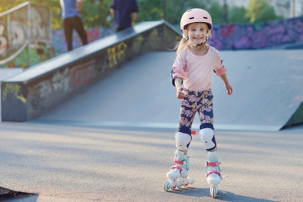 Mooi meisje op rolschaatsen in een helm en bescherming van handen en voeten in een skatepark