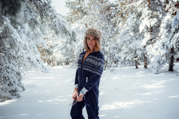 Mooi meisje permanent, in de winter in bospark, achtergrond van kerstboom sneeuw, ze rust in resort. Vrije ruimte voor tekst. Blauwe jumpsuit om te sporten.