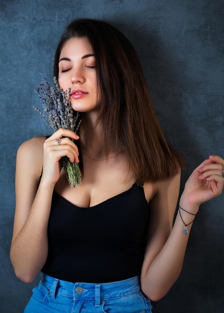 Mooi meisje poseren in de studio op een donkere achtergrond Ze houdt een klein boeket lavendel in haar handen Close-up portret