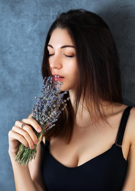 Foto mooi meisje poseren in de studio op een donkere achtergrond ze houdt een klein boeket lavendel in haar handen close-up portret