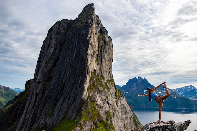 mooi meisje strekt zich uit (yoga - danserespositie) op rotsen met uitzicht op de beroemde segla-berg, noorwegen