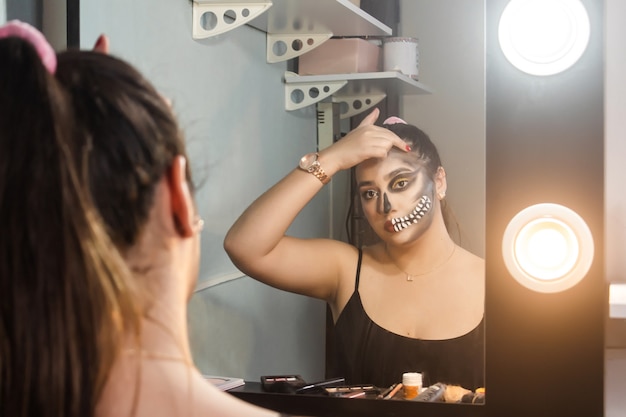 Mooi meisje vervaagt haar make-up van een artistieke schedel voor halloween in haar kamer.