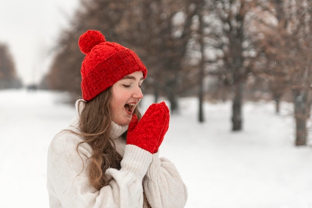 Mooi meisje verwarmt haar handen in rode wanten wandelen in het besneeuwde park Vrouw in gebreide goederen in de winter binnen buiten