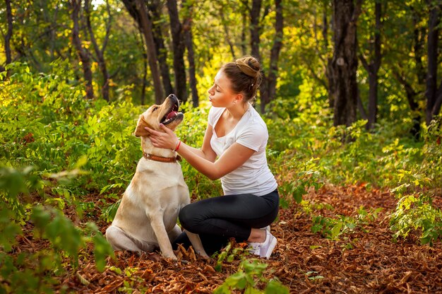 mooi meisje zit in het bos met een hond en haar geliefde huisdier aaien