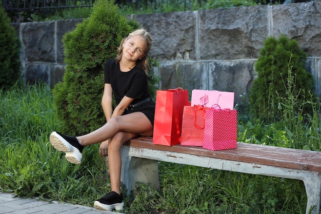 Mooi meisje zit op een bankje in het park met gekleurde tassen