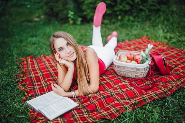 Mooi meisje zittend op de plaid in het park en het lezen van boek.