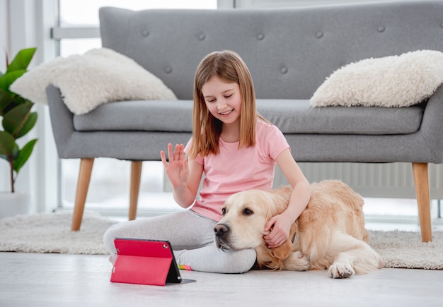 Mooi meisje zittend op de vloer met golden retriever hond en praten met familie vrienden online op tablet