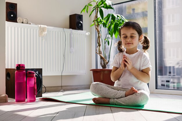 Mooi meisje, zittend op een fitness-mat en het beoefenen van yoga in lotushouding tegen de achtergrond