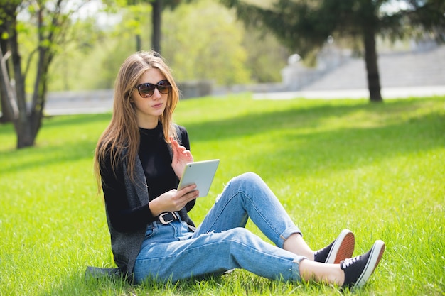 Mooi meisje, zittend op het gras met tablet tijdens de zomer.