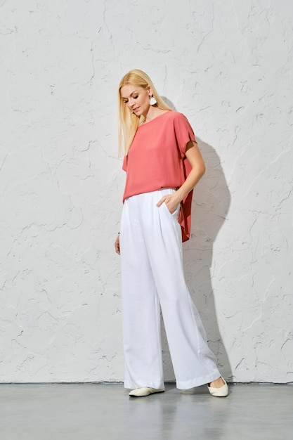 Mooi model in roze shirt en witte wijde katoenen broek poserend onder fel licht