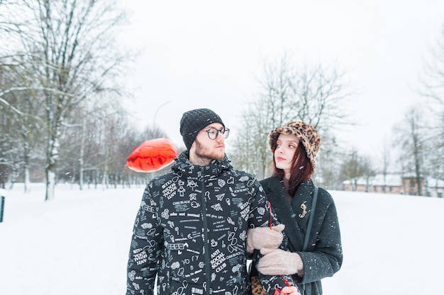 Mooi modieus jong koppel in stijlvolle winterkleding met een rode ballon loopt in een park met sneeuw